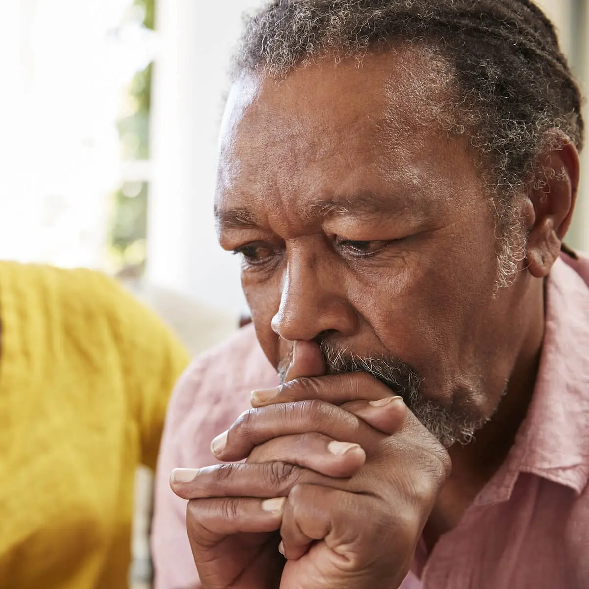 A senior African American man leans forward and holds his hands to his mouth
