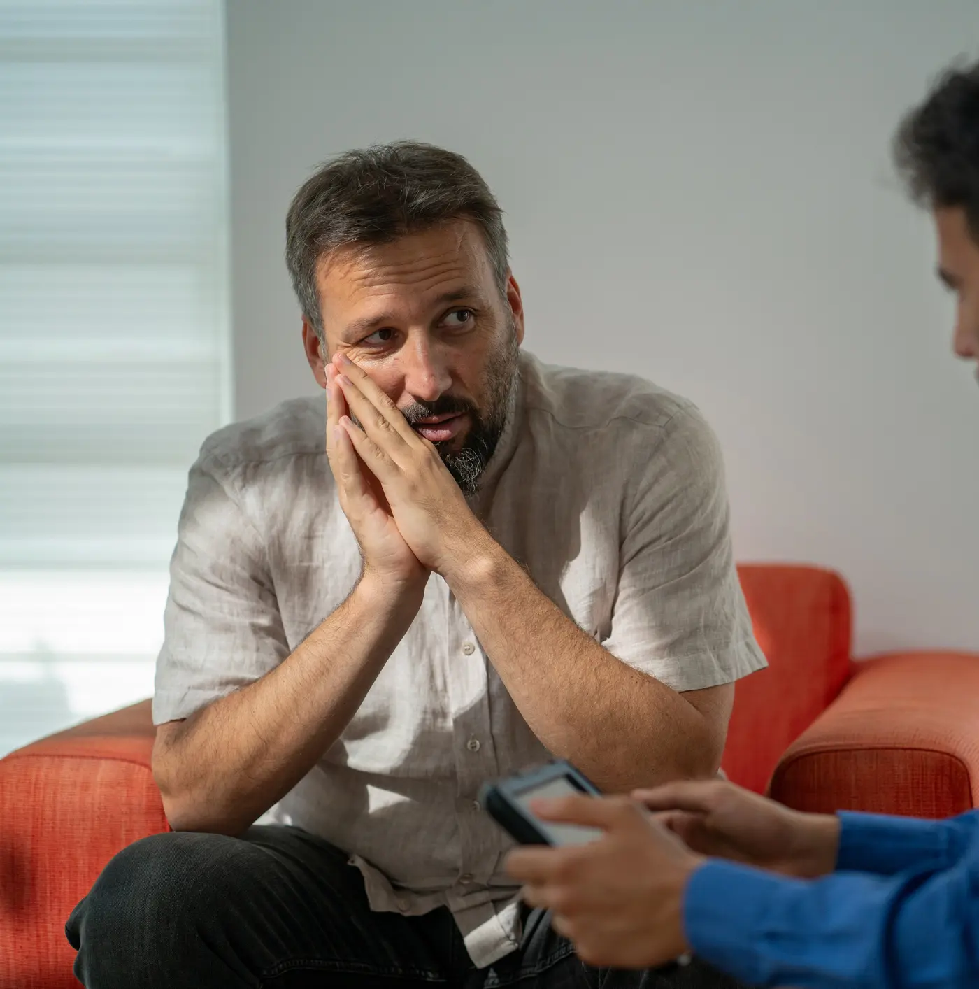 Worried man leans forward in his seat as he looks toward a partially unseen male therapist
